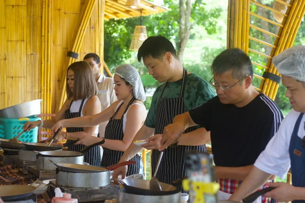 Master Thai Cuisine Visitors preparing Thai dishes at a row of cooking stations