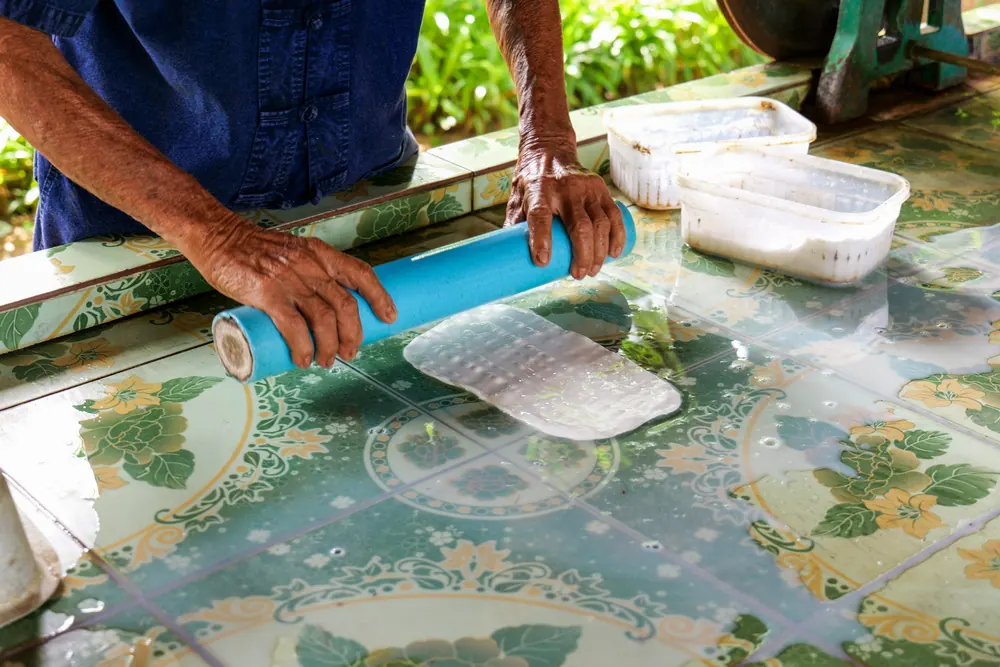 Learning Rubber Tapping A guide rolling a sheet of natural rubber during a farm demonstration